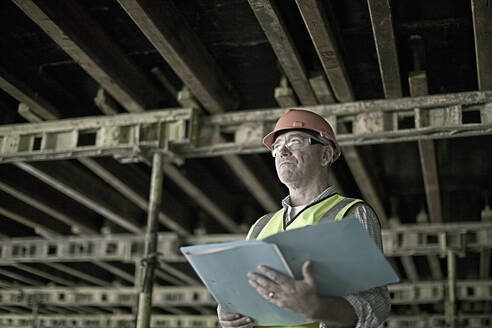 Porträt eines Bauarbeiters auf einer Baustelle mit Plänen in der Hand - AJOF01198