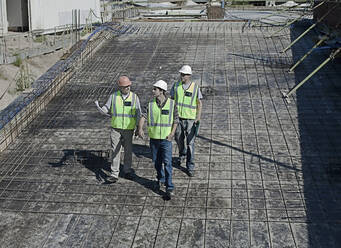 Three male construction workers walking and talking at construction site - AJOF01201