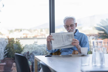 Älterer Mann liest Zeitung, während er zu Hause am Tisch sitzt - EIF00419