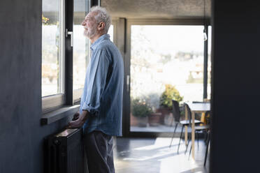 Smiling man looking through window while standing at home - EIF00432