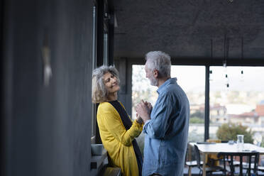 Senior man holding hand of woman while standing by window at home - EIF00435