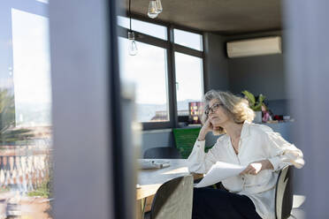 Contemplating woman sitting with paper on chair at home - EIF00465