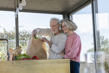 Smiling woman standing by man unpacking vegetable at home - EIF00468