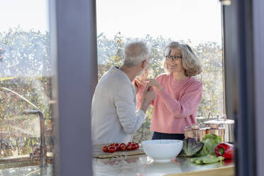 Senior woman feeding man while standing at home - EIF00471