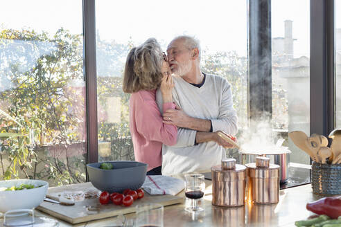 Senior couple kissing each other while standing by kitchen island at home - EIF00478