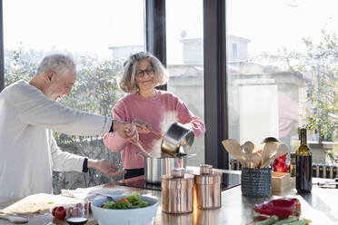 Senior couple cooking together while standing in kitchen at home - EIF00481