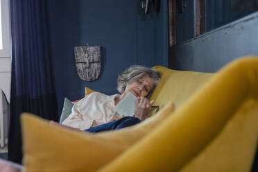 Woman reading book while sitting on sofa at home - EIF00499