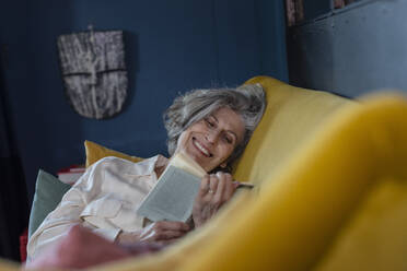 Senior woman smiling while reading book at home - EIF00500