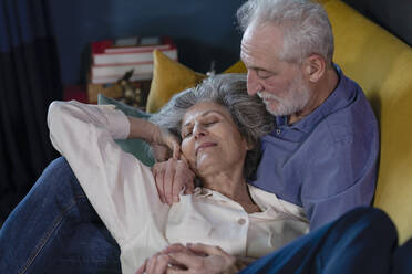 Smiling woman resting on senior man lap at home - EIF00507