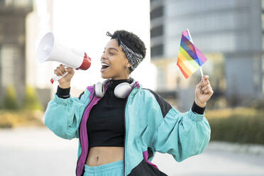 Weibliche LGBTQIA-Demonstrantin hält Regenbogenfahne, während sie durch Megaphon verkündet - JCCMF01332