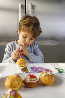 Süßer Junge dekoriert Muffin am Küchentisch - IFRF00437