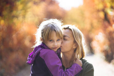 Mother kissing cute daughter on cheek in park - PSIF00451