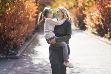 Smiling mother carrying daughter while walking in park - PSIF00452