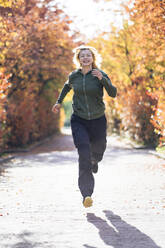 Cheerful mature woman running in park on sunny day - PSIF00453