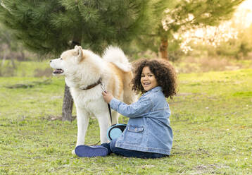 Smiling boy sitting by dog on grass in nature - JCCMF01342
