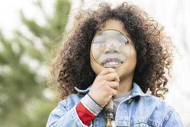 Cute boy holding magnifying glass in front of face - JCCMF01343