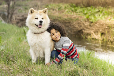 Lächelnder Junge schaut weg, während er sich in der Natur an einen Hund lehnt - JCCMF01346
