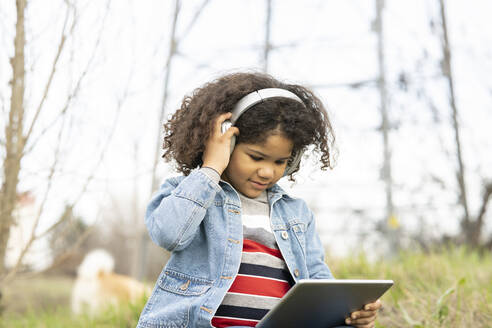 Boy listening through headphones while using digital tablet in nature - JCCMF01355