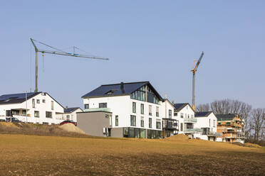 Deutschland, Baden-Württemberg, Waiblingen, Moderner energieeffizienter Vorort mit Industriekränen im Hintergrund - WDF06537