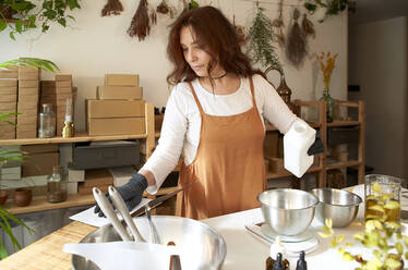 Woman looking at recipe while measuring ingredient for making soap in workshop - VEGF04014