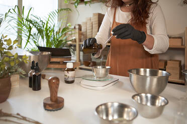 Frau gießt ätherisches Öl in eine Schale zur Herstellung von Seife in einer Werkstatt - VEGF04018