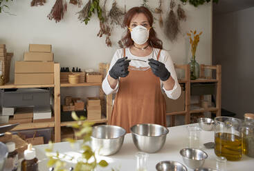 Frau mit Gesichtsschutzmaske und Brille bei der Herstellung von Seife in einer Werkstatt - VEGF04024