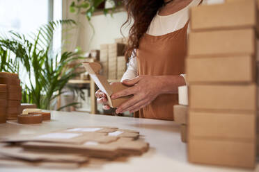 Frau verpackt Seife in braunen Schachteln in einer Werkstatt - VEGF04034