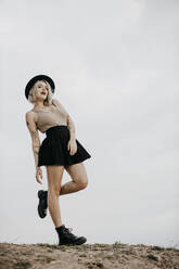 Junge Frau mit Hut steht auf einem Bein gegen den Himmel - GMLF01040