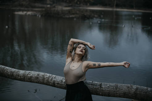 Young woman leaning on fallen tree against lake - GMLF01045