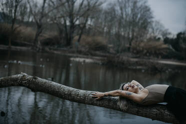 Frau auf umgestürztem Baum am See liegend - GMLF01047