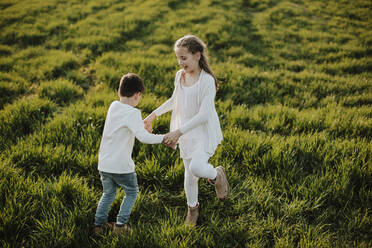 Boy and girl holding hands while playing on grass during sunny day - GMLF01054