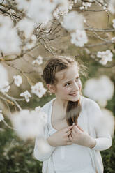 Fröhliches Mädchen schaut weg, während es an einem Mandelbaum steht - GMLF01063