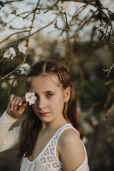 Girl staring while standing by almond tree during sunset - GMLF01069