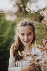 Nettes Mädchen lächelt, während es neben Mandelbaumblüten steht - GMLF01073