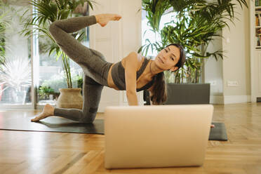 Female yoga instructor exercising during online class through laptop - GMCF00087