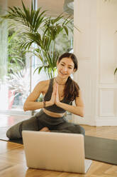 Lächelnde Yogalehrerin, die während eines Online-Kurses über einen Laptop grüßt - GMCF00089