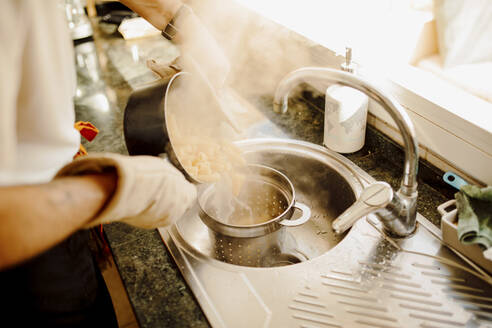 Junger Mann gießt kochendes Wasser aus einem Kochtopf auf Nudeln in einem Sieb - GMCF00094