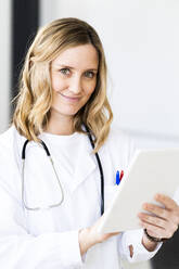 Lächelnde blonde Ärztin mit digitalem Tablet in einer medizinischen Klinik - GIOF11619