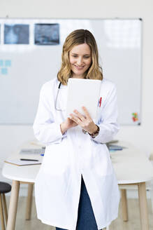 Lächelnder medizinischer Angestellter, der ein digitales Tablet benutzt, während er am Schreibtisch steht - GIOF11622