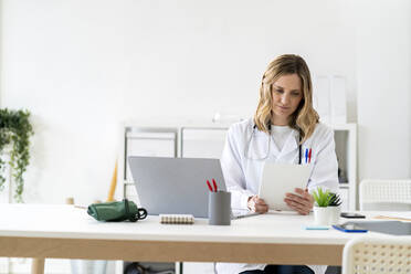 Mitarbeiterin des Gesundheitswesens benutzt ein Tablet, während sie am Schreibtisch in einer medizinischen Klinik sitzt - GIOF11628