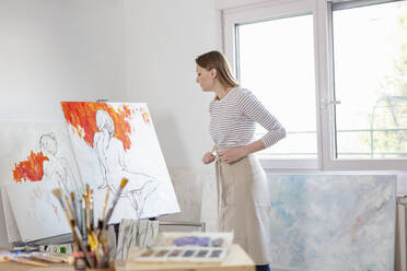 Female artist looking at canvas in home studio - EIF00529