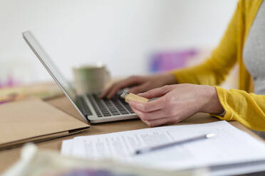 Mid adult woman holding USB stick by laptop on table at home - EIF00548