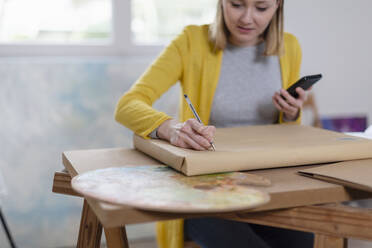 Malerin schreibt auf Lieferpaket im Heimstudio - EIF00555