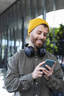 Lächelnder Mann mit Smartphone am Gebäude - PNAF00906