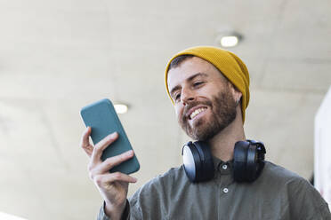 Lächelnder Mann mit Strickmütze, der im Freien stehend ein Smartphone benutzt - PNAF00910