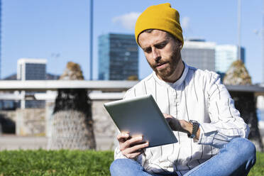 Handsome man using digital tablet while sitting at park during sunny day - PNAF00915