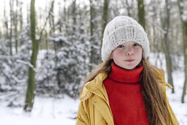 Mädchen mit Strickmütze, das bei Schnee an einem Baum steht - OGF00931