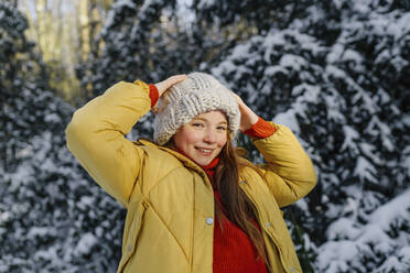 Smiling girl in yellow jacket standing against snowy trees - OGF00933