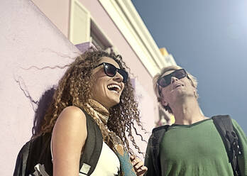 Cheerful man and woman laughing while looking away on sunny day - AJOF01215