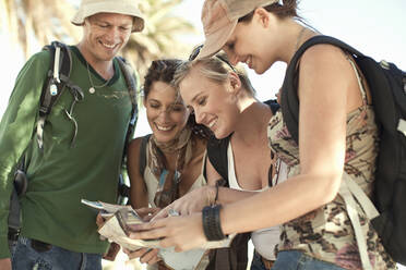 Lächelnde männliche und weibliche Touristen, die an einem sonnigen Tag eine Landkarte betrachten - AJOF01227